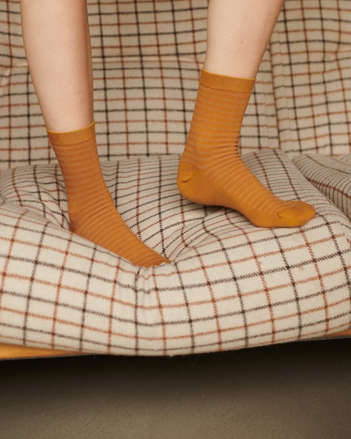 Person standing on a sofa with orange striped organic cotton socks